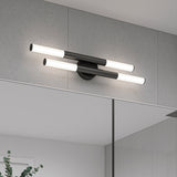 Modern wall-mounted light fixture with two horizontal black bars, each with white cylindrical ends, installed above a bathroom mirror on a gray tiled wall. Part of a plant is visible in the lower left corner.