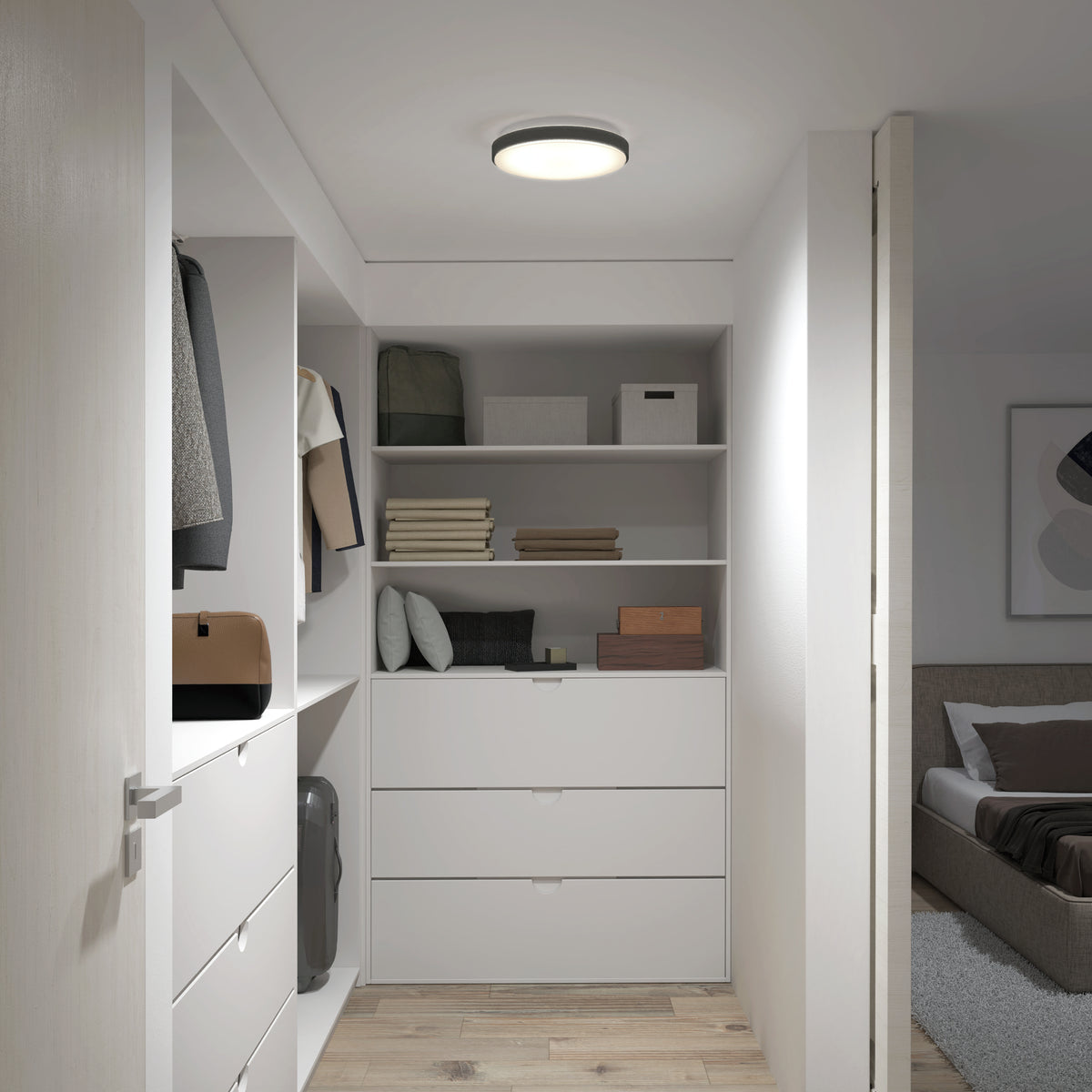 A modern walk-in closet with white shelves, neatly folded clothes, boxes, and a few hanging jackets. The space is well-lit and leads into a bedroom with a bed and a rug visible through an open door.