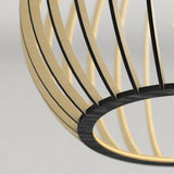 Close-up of a modern, minimalist lampshade with thin, curved, gold and black metal bars against a light gray background. The design creates an open, spherical structure.