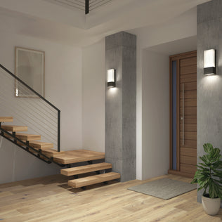 Modern entryway with floating wooden stairs, metal railing, a wooden door, concrete accent columns featuring Artikas Dixon indoor-outdoor LED wall light, light wood flooring, framed picture, doormat, and a potted plant in the corner.