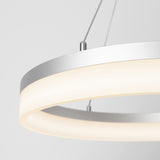 Close-up of a modern circular pendant light with a metallic frame and soft, diffused white illumination, suspended by thin cables against a plain light gray background.