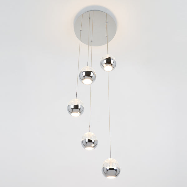 The Artika Oracle modern 5-light LED pendant features five chrome-finished spheres hanging at varying lengths, casting white light against a plain white background.