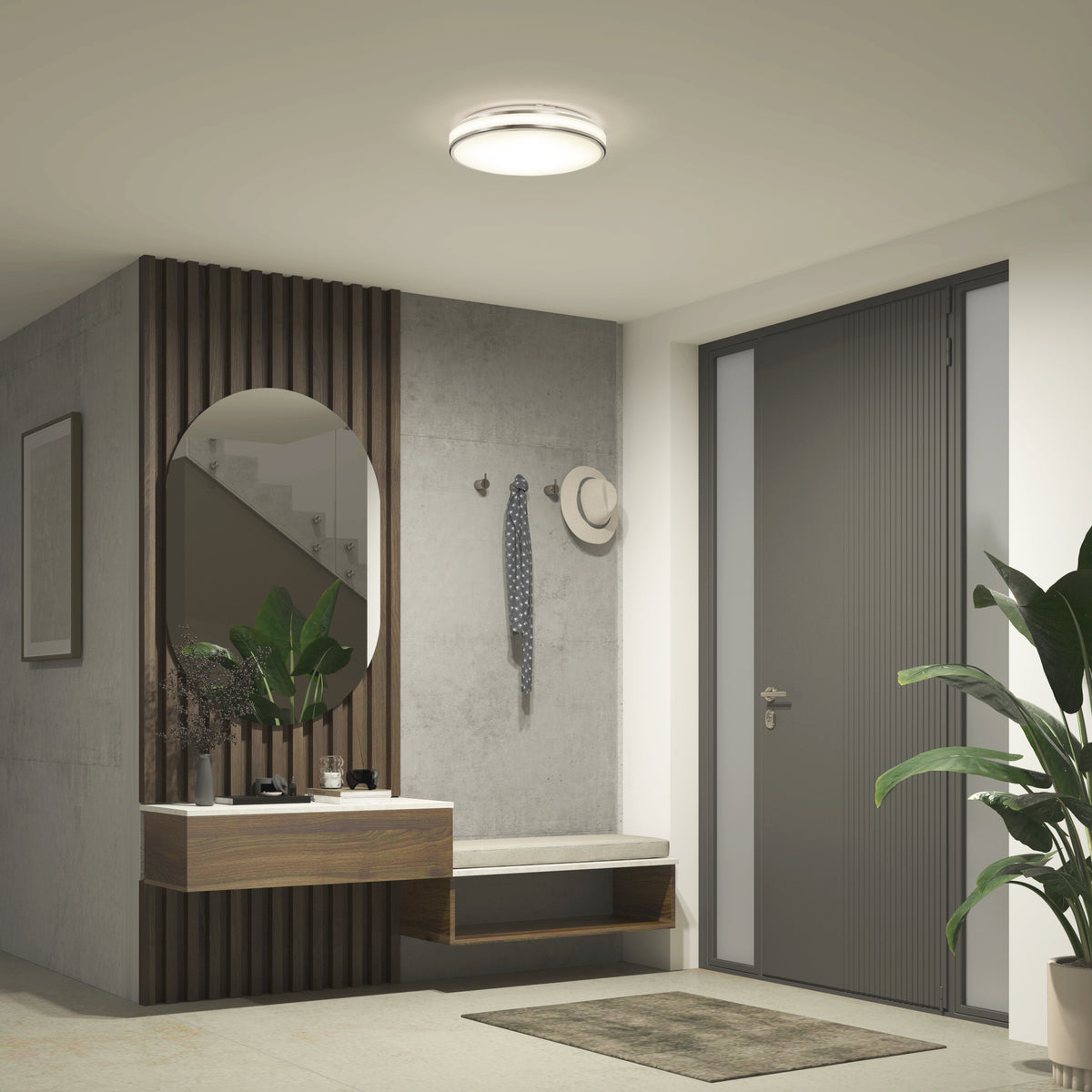 Modern entryway with a gray door, round mirror above a wooden floating shelf, small bench, hooks with hat and scarf, green potted plant in the corner, and brightened by the Artika Hemisphere 15 in. LED flush mount light 5 CCT.