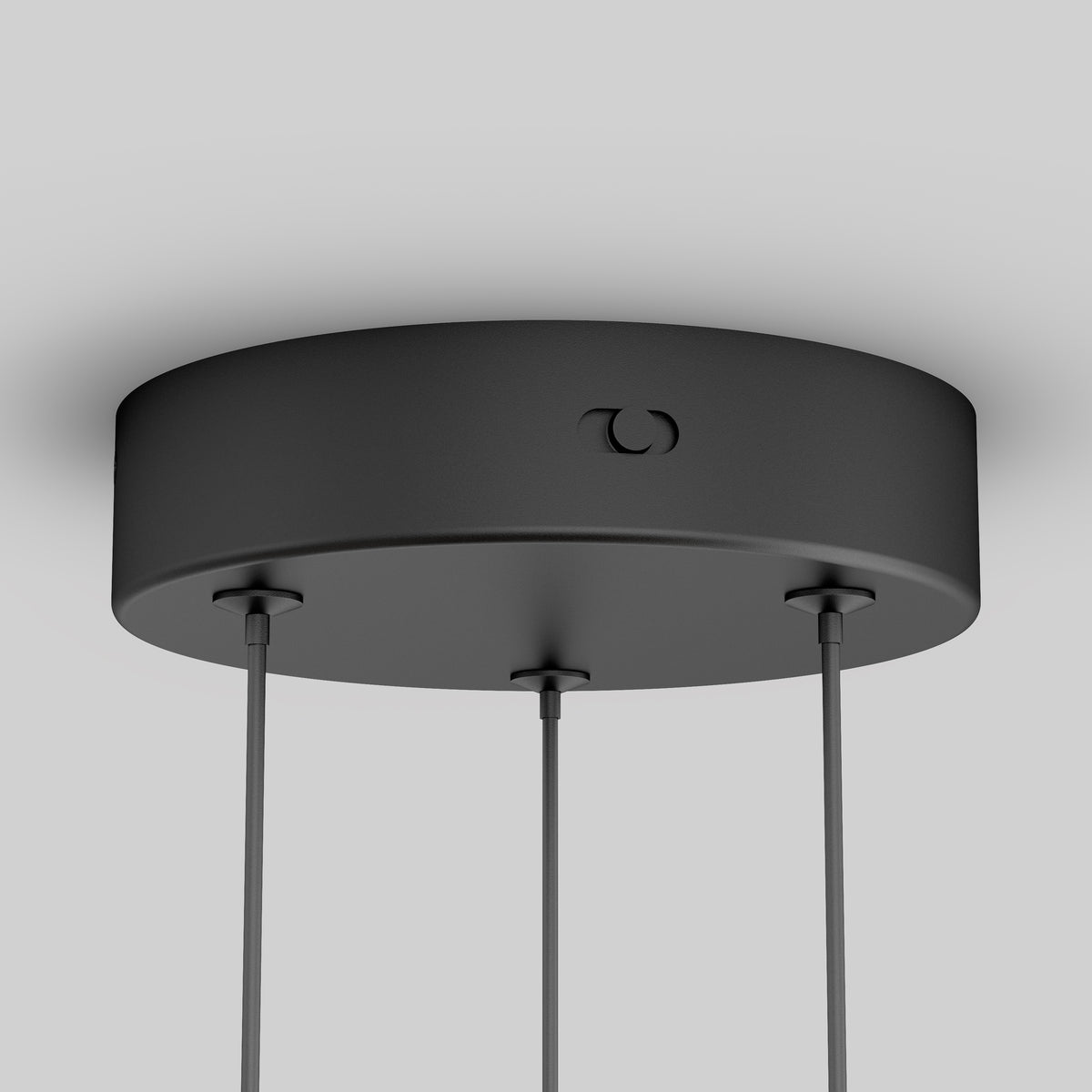 A close-up view of a round, black ceiling canopy with three cables suspended from it, set against a plain light gray background.