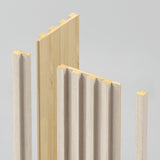 Four vertical wooden panels with tongue and groove edges are arranged upright against a plain, light gray background. The panels have a light wood finish, with one panel displaying a flat surface and others featuring a slatted design.