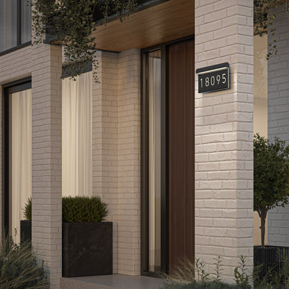 Modern house entrance featuring white brick walls, large windows with white curtains, a dark wood door, a rectangular planter with greenery, and the Artika Bowen modern LED outdoor address wall light (5 CCT) displaying 18095.