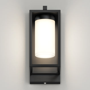 The Artika Aurel Outdoor LED Light, 3CCT, features a modern black rectangular frame with a cylindrical frosted glass fixture, mounted on a light gray wall and emitting a soft, even glow.