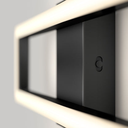 A close-up of the Artika-CAN-dev Dover modern LED bathroom vanity light 5 CCT, a sleek rectangular black fixture with soft white LED lighting around its frame, mounted on a light gray wall in a minimalist style.