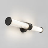 A modern wall-mounted light fixture with a cylindrical, ribbed glass shade and black metal accents, glowing softly against a plain light gray wall.