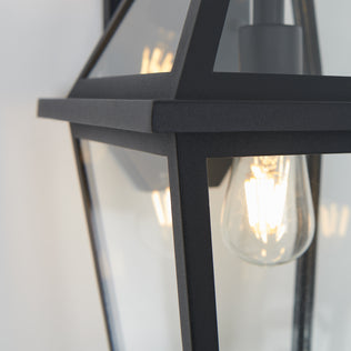 Close-up of the Artika Colonial outdoor lantern wall light, featuring black metal and glass with a vintage-style exposed filament bulb, mounted on a light-colored wall.