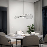A modern dining room with a round marble table set for a meal, surrounded by gray upholstered chairs. A contemporary black wire pendant light hangs above, and a potted plant is by the window with floor-length curtains.