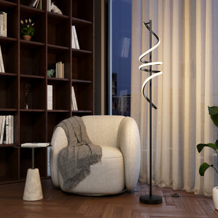 A cozy, rounded white armchair with a gray blanket sits next to the Artika Coda modern LED floor lamp 5CCT in a stylish room featuring wood floors, built-in bookshelves, and large windows with sheer curtains.