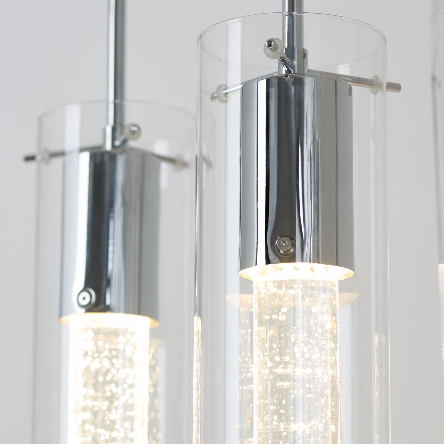 Close-up of Artikas Bubble Flow 4-light pendant, featuring cylindrical glass shades with chrome fixtures; illuminated lights reveal small bubbles inside the inner glass tubes, creating a sparkling effect.