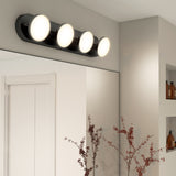 A modern bathroom with a black vanity light fixture featuring four round, illuminated bulbs mounted above a large mirror. There are shelves with bottles and decorative branches in a vase on the counter.
