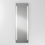 A tall rectangular mirror mounted on a white wall, featuring two vertical LED light strips on either side, emitting a bright white glow.