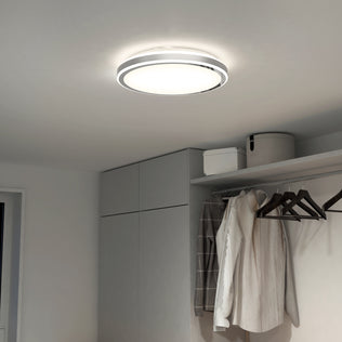 The Artika Altitude 15 in. LED modern flush mount light with 5 CCT settings illuminates a minimalist room featuring gray cabinets, a closet with hanging clothes, and storage boxes on the upper shelf.