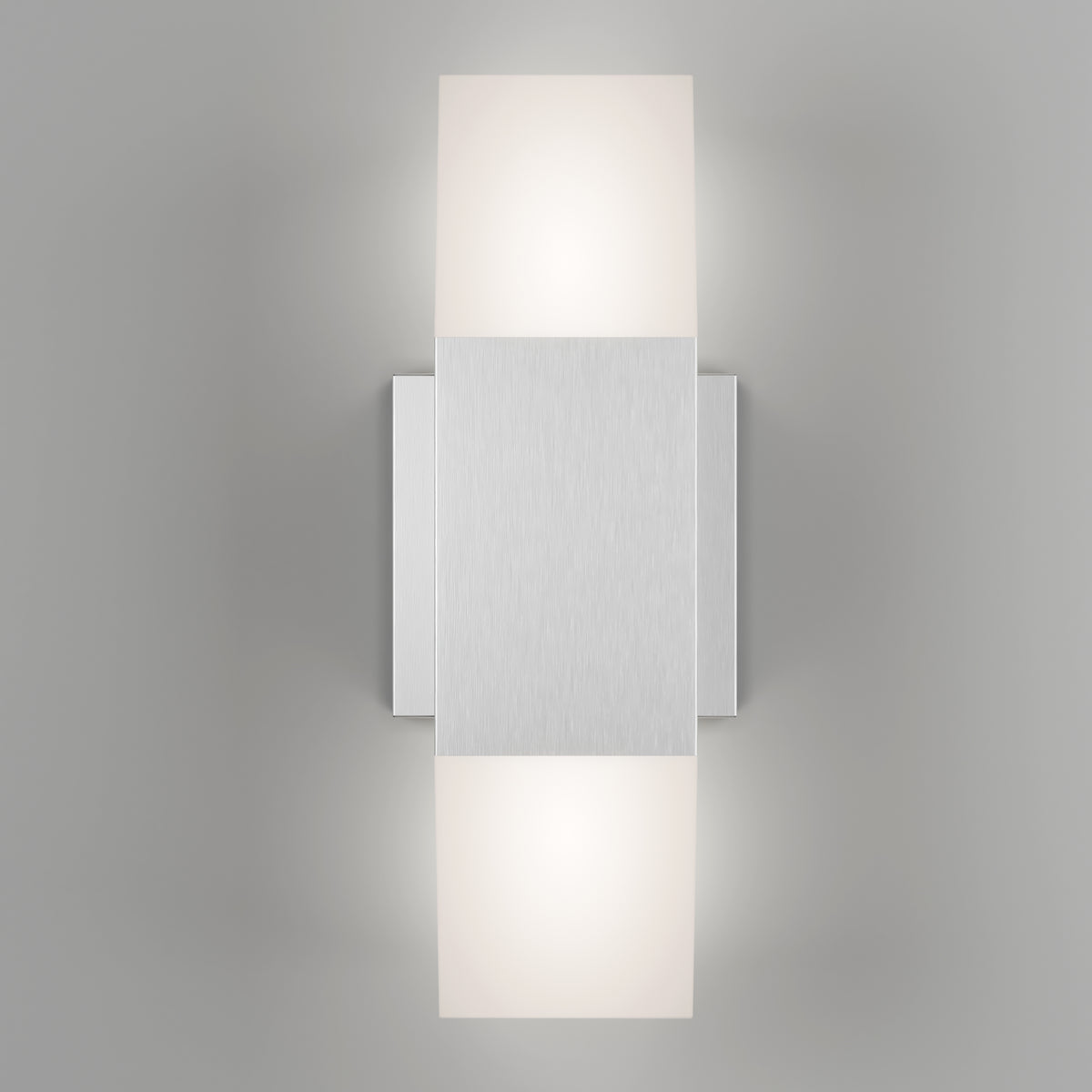 A modern wall sconce with a brushed metal rectangular center and two frosted light diffusers above and below, casting a soft glow on a light gray wall.