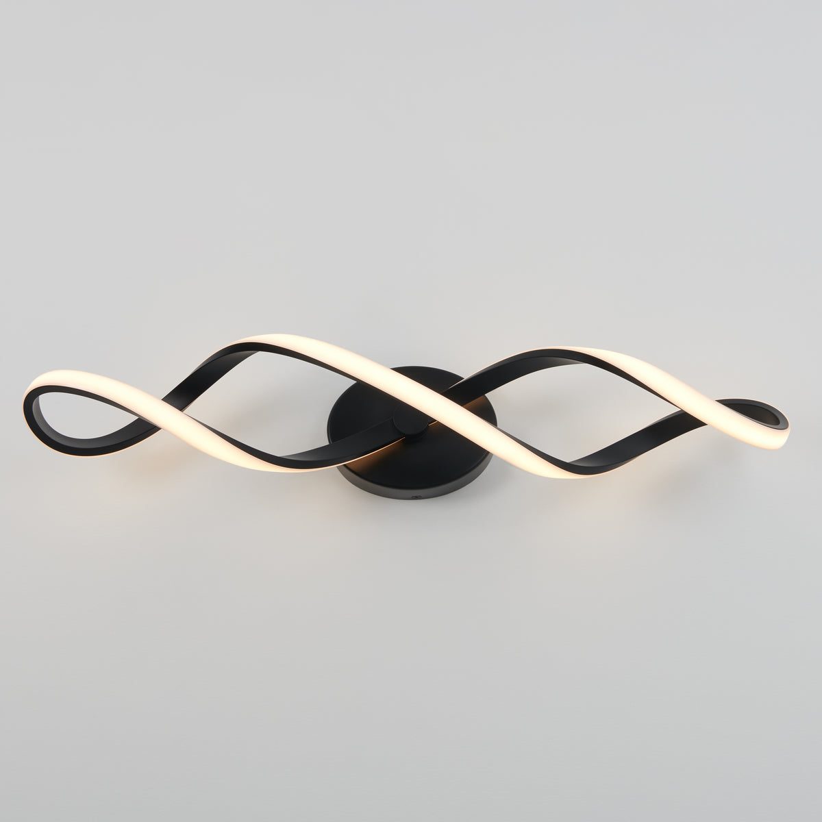 A modern wall light fixture with two intertwined, wave-like LED strips—one illuminated white, one dark—mounted on a round black base against a plain gray background.
