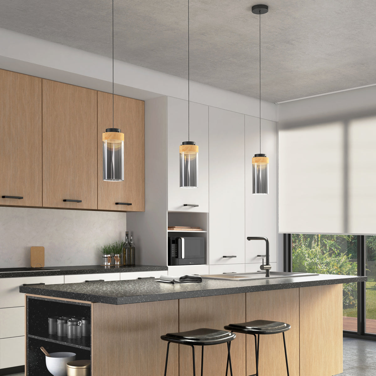 Modern kitchen with light wood cabinets, a large island with black countertop, two black stools, three Artika Hanson 1-light LED pendant lights above, and a large window with a roller shade letting in natural light.