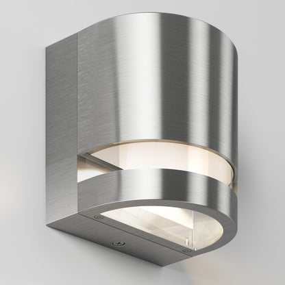The Artika Valor Round LED indoor-outdoor wall light features a modern curved design with a brushed metal finish and frosted glass cover, mounted on a light gray wall.