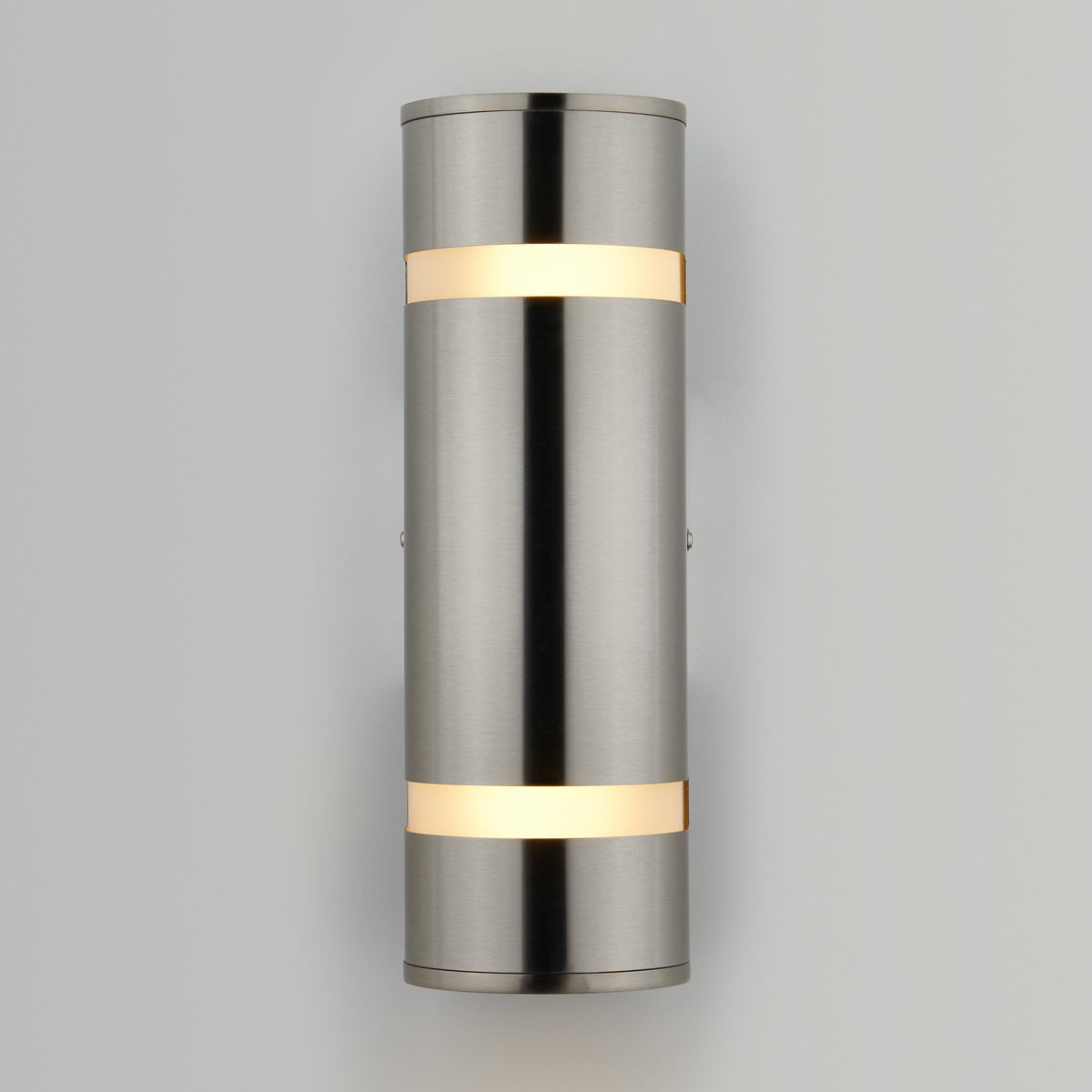 The Artika Q1 indoor-outdoor wall light features a modern cylindrical design with a brushed metal finish and two horizontal bands, emitting warm white light at the top and bottom, mounted on a plain light gray wall.