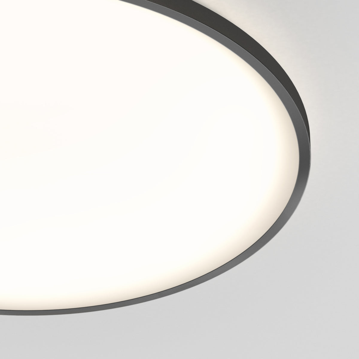 A close-up view of a round ceiling light fixture with a black rim, emitting a soft, even white glow against a plain light gray ceiling.