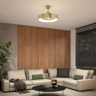 A modern living room with a beige sectional, green and black cushions, round black coffee table, wood-paneled walls, potted plant, and the Artika Austin 23 in. LED modern ceiling fan with remote. Large windows feature black blinds.