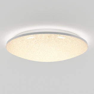 The Artika Sparkle LED flush mount light features a round, textured surface and emits a warm, even glow. Mounted on a white ceiling, this modern fixture comes with a remote for easy control.