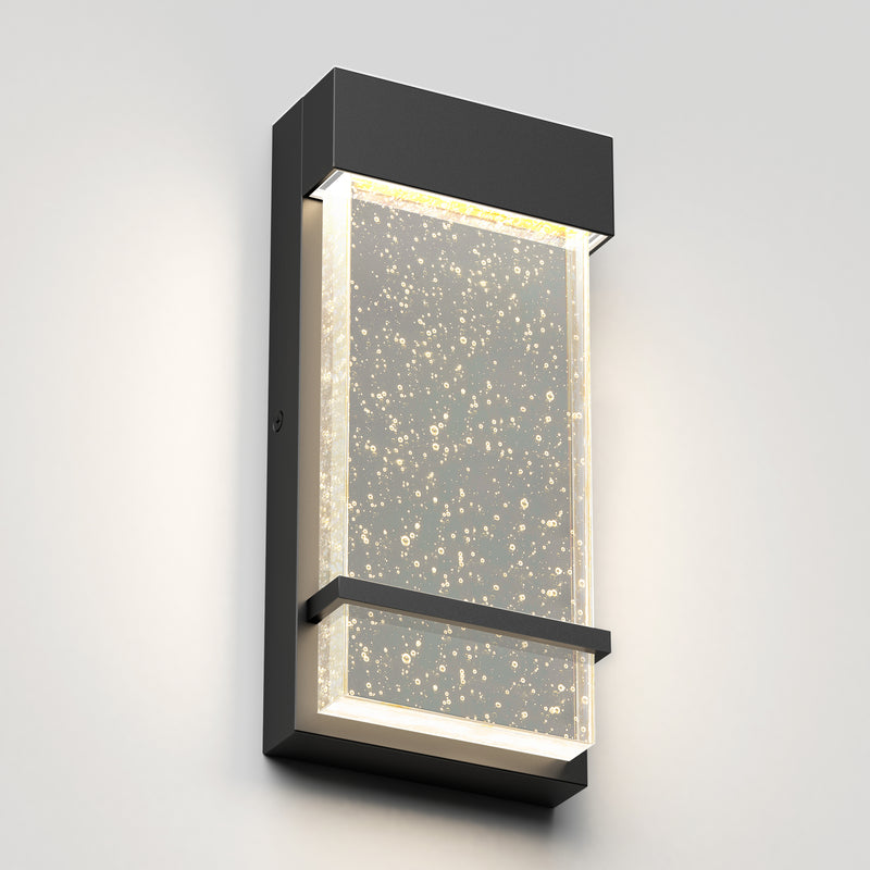The Skyler indoor-outdoor LED wall light by Artika features a modern rectangular black metal frame and a clear textured panel with bubble details, casting soft white light while mounted on a light gray wall.