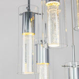 Close-up of modern pendant lights with cylindrical glass shades and inner LED tubes featuring bubble-like details, emitting a soft, warm glow against a light background.