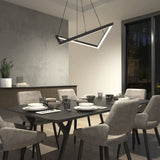 A modern dining room with a rectangular black table set for six, surrounded by cushioned gray chairs. A geometric chandelier hangs above, and a large window and potted plant are visible in the background.