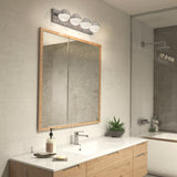 Modern bathroom with a large wood-framed mirror above a white countertop, single sink, soap dispenser, small plant, and a row of decorative lights above the mirror. A shower is visible in the reflection.