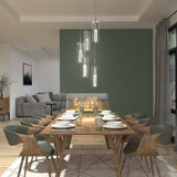 A modern dining room with a wooden table set for eight, green upholstered chairs, pendant lights above, and a glass fireplace separating the dining area from a gray living room. Large windows let in natural light.