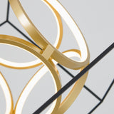 Close-up of a modern light fixture featuring intersecting golden rings with integrated LED lights, set against a plain light gray background. The design appears geometric and contemporary.