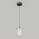 A modern pendant light fixture with a cylindrical glass shade, featuring a cluster of small lights inside, hangs from a black cord attached to a round ceiling mount against a plain light gray background.
