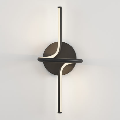 The Artika Swirl LED Sconce features a circular black base and two curved vertical light bars crossing at the center, mounted on a white wall and emitting a soft, warm glow.