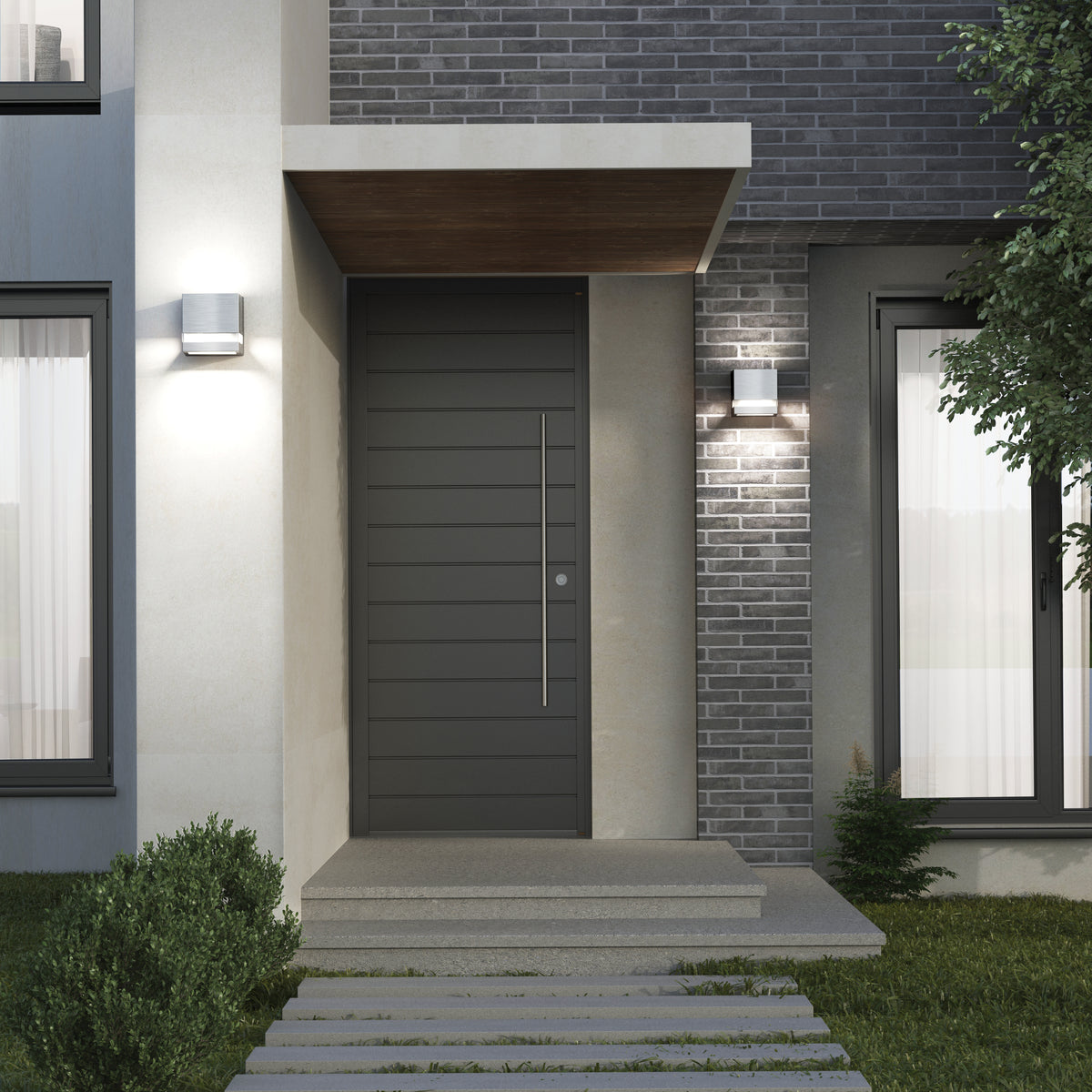 Modern house entrance with a dark gray front door, horizontal panels, and a vertical handle. Gray brick and light concrete walls, outdoor wall lights, large window with curtains, and green shrubs line the walkway.
