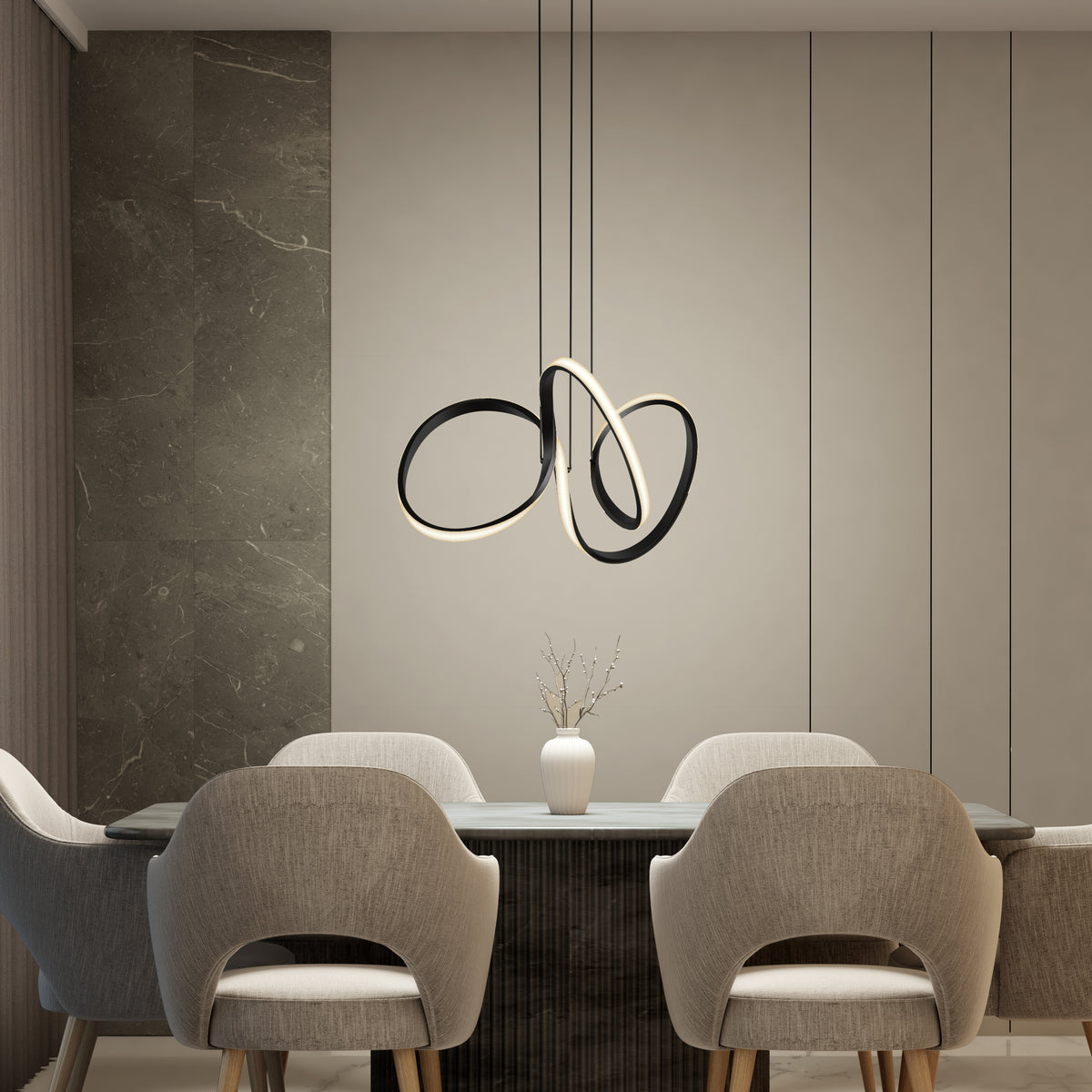 A modern dining area with four gray upholstered chairs around a rectangular table. A minimalist white vase with branches sits on the table, and a sculptural pendant light hangs from the ceiling. The background features neutral-toned walls.