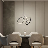 A modern dining area with four gray upholstered chairs around a rectangular table. A minimalist white vase with branches sits on the table, and a sculptural pendant light hangs from the ceiling. The background features neutral-toned walls.