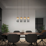 A modern dining room with a wooden table, six dark upholstered chairs, four pendant lights hanging above, a potted plant in the corner, and large windows with city views at night.