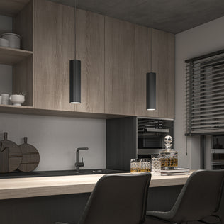 A modern kitchen features wood cabinets, two counter chairs, partially closed blinds on the right, and a decanter with glasses. Above, the Artika Groove LED modern pendant light 3 CCT provides stylish illumination.