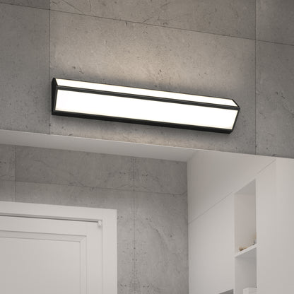 The Artika Preston LED modern bathroom vanity light 3 CCT, a sleek rectangular wall fixture with black edges, is mounted above a white door and open shelves on a gray tiled wall.