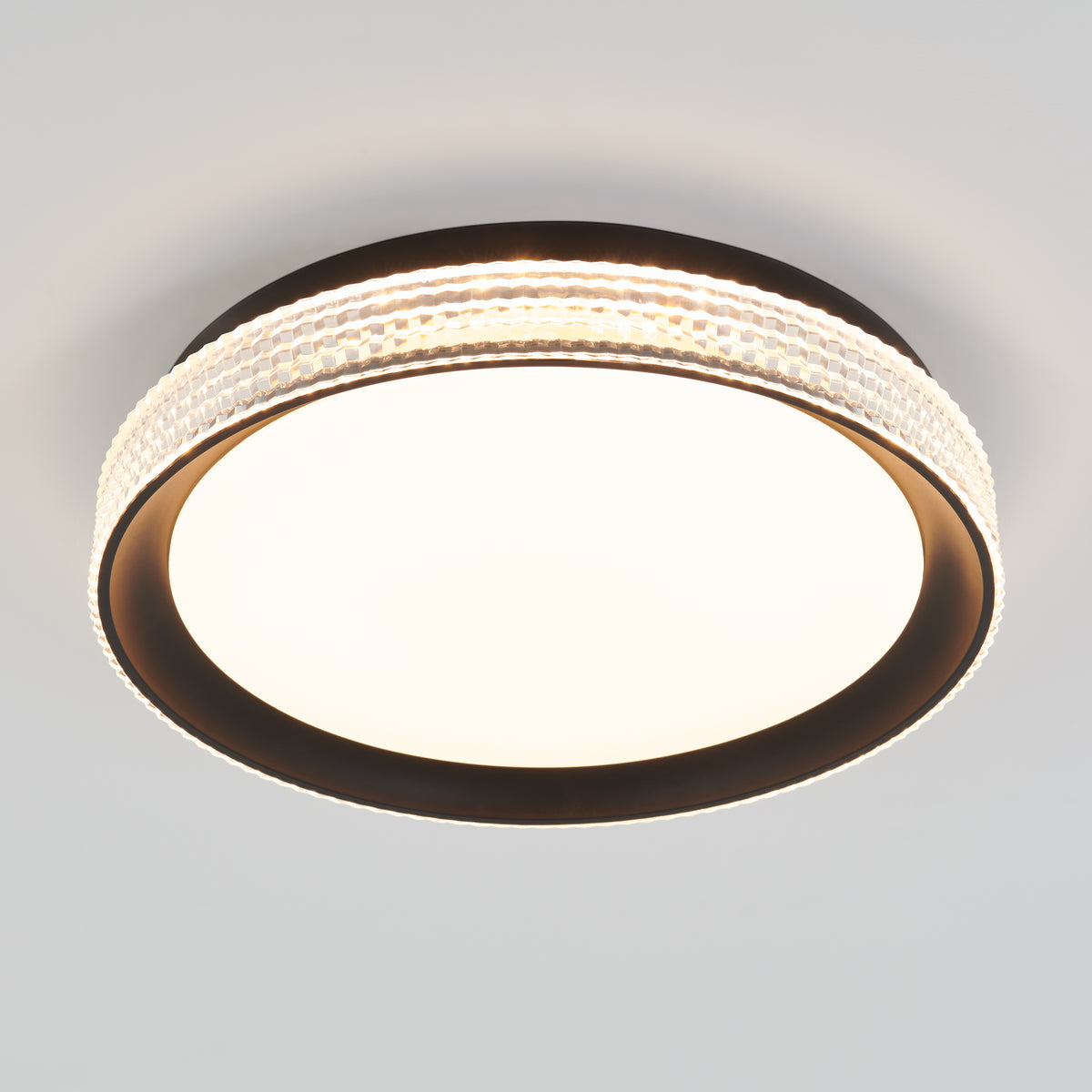 A round ceiling light fixture with a dark outer rim, a wide illuminated center, and a decorative band of textured, clear material encircling the edge, mounted on a white ceiling.