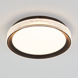 A round ceiling light fixture with a dark outer rim, a wide illuminated center, and a decorative band of textured, clear material encircling the edge, mounted on a white ceiling.