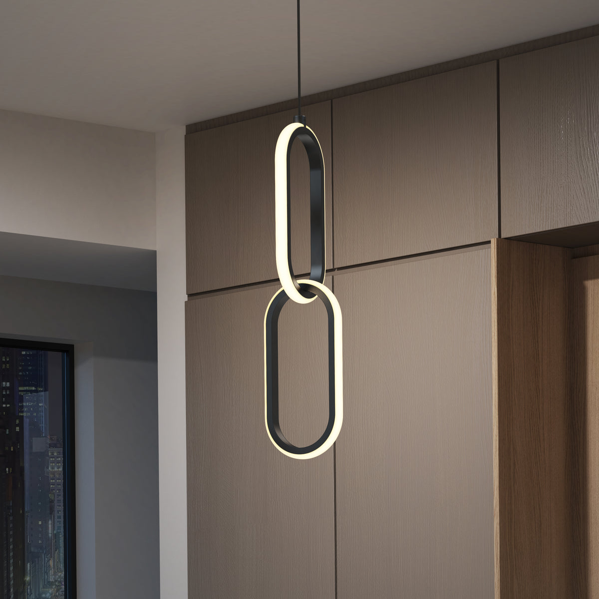 A modern, oval-shaped pendant light with two linked illuminated rings hangs from the ceiling in front of wood-paneled cabinets, with a cityscape visible through a window at night.