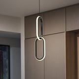A modern, oval-shaped pendant light with two linked illuminated rings hangs from the ceiling in front of wood-paneled cabinets, with a cityscape visible through a window at night.