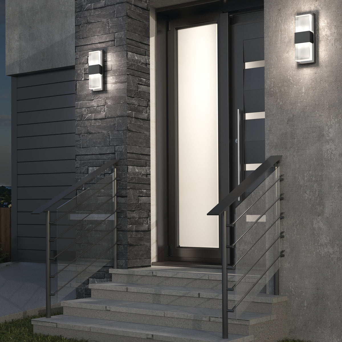 Modern front entrance with stone and concrete walls, metal railing on stairs, frosted glass door, and two rectangular outdoor wall lights glowing in the evening.