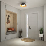 Modern entryway with a built-in wooden bench, gray cushion, and throw pillows, wall hooks holding jackets, a round jute rug, potted plant, umbrella stand, and a contemporary front door letting in natural light.