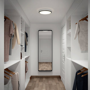 A modern walk-in closet with hanging clothes and shelves, lit by the Artika Vera 13 in. Modern LED Flush Mount Ceiling Light.