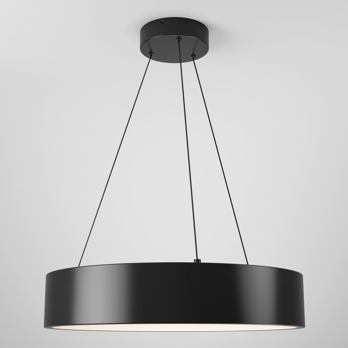 A modern, circular black pendant light hangs from the ceiling by four thin black cables, emitting a soft white glow from its underside against a plain white background.